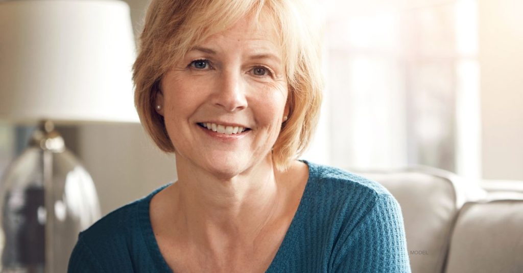 mature female (model) looks into the camera while sitting on her couch